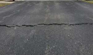 A wide transverse crack running horizontally across the width of an aging asphalt driveway pavement.