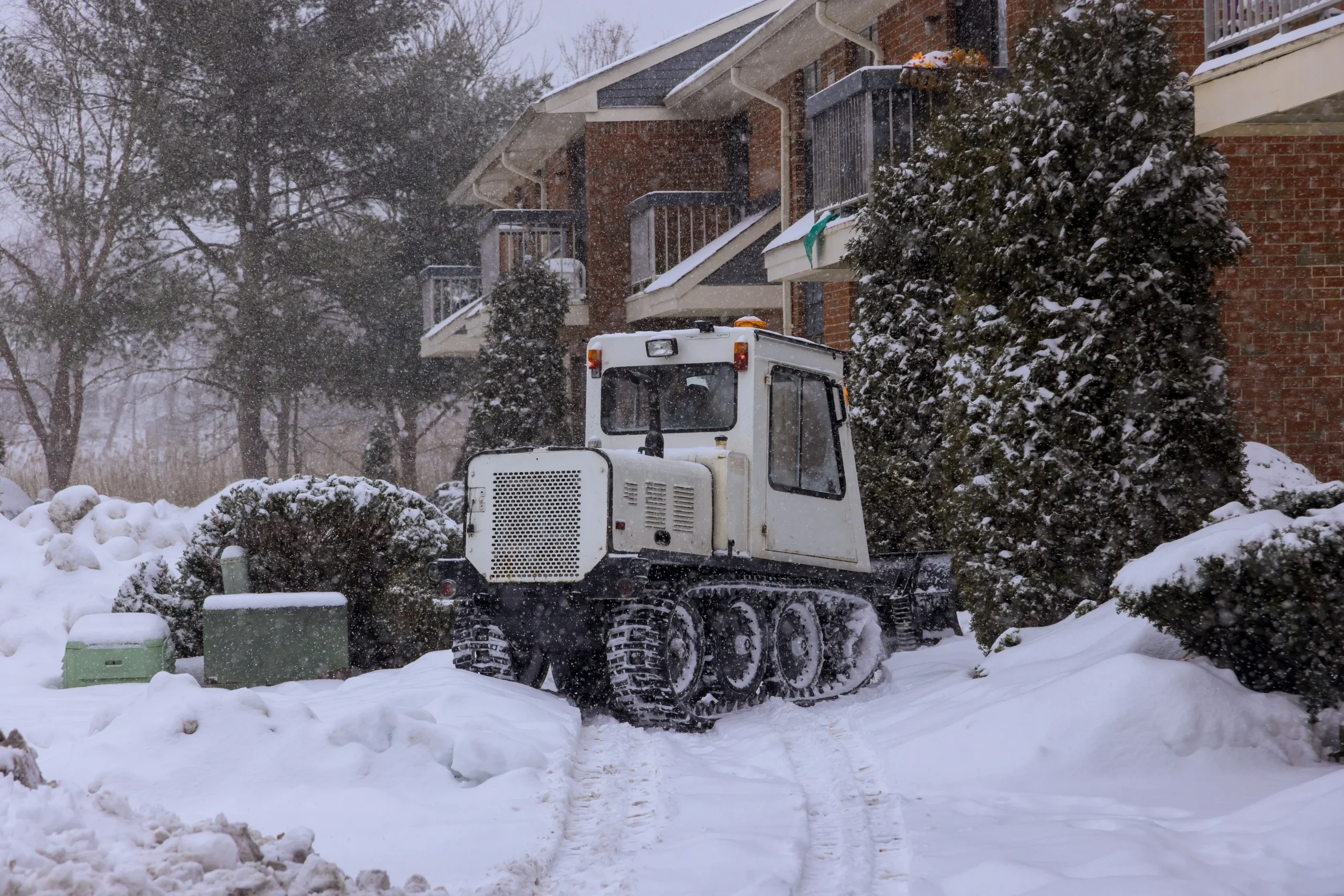 Compact tracked snow-removal vehicle clearing paths near residential buildings