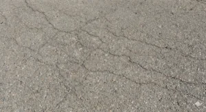 Close-up of fine hairline cracks on a gray asphalt surface.
