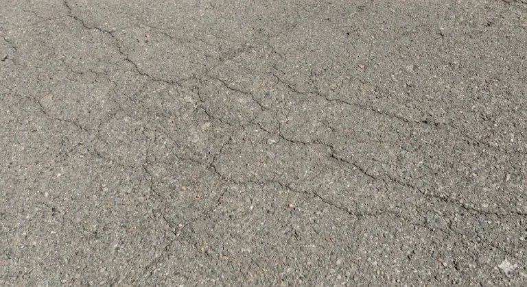 Close-up of fine hairline cracks on a gray asphalt surface.