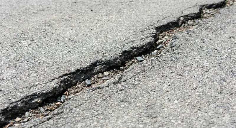 A large horizontal transverse crack extending across the entire width of a residential asphalt driveway.