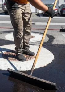 Contractor manually applying dark asphalt sealcoat with a squeegee in Treasure Valley, Idaho.